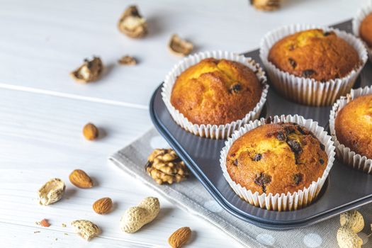 Vanilla caramel muffins in paper cups on white wooden background. Delicious cupcake with raisins, almonds and nuts. Homemade biscuit cakes. Copy space for text.