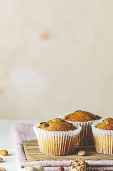 Vanilla caramel muffins in paper cups on white wooden background. Delicious cupcake with raisins, almonds and nuts. Homemade biscuit cakes. Copy space for text.