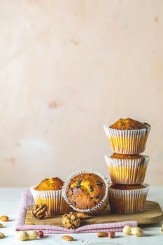 Vanilla caramel muffins in paper cups on white wooden background. Delicious cupcake with raisins, almonds and nuts. Homemade biscuit cakes. Copy space for text.