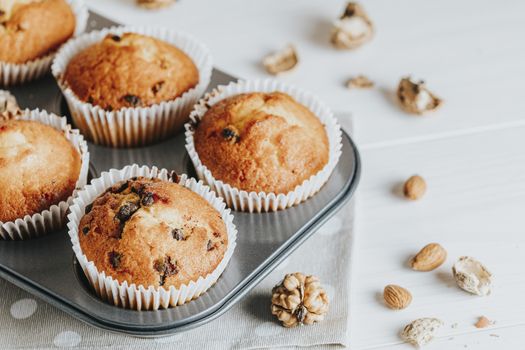 Vanilla caramel muffins in paper cups on white wooden background. Delicious cupcake with raisins, almonds and nuts. Homemade biscuit cakes. Copy space for text.