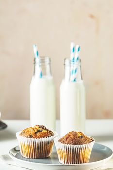 Vanilla caramel muffins in paper cups and bottles of milk on white wooden background. Delicious cupcake. Homemade biscuit cakes. Copy space for text.