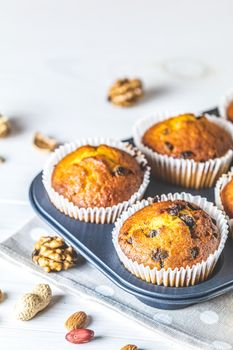 Vanilla caramel muffins in paper cups in bakeware on white wooden background. Delicious cupcake with raisins, almonds and nuts. Homemade biscuit cakes. Copy space for text.