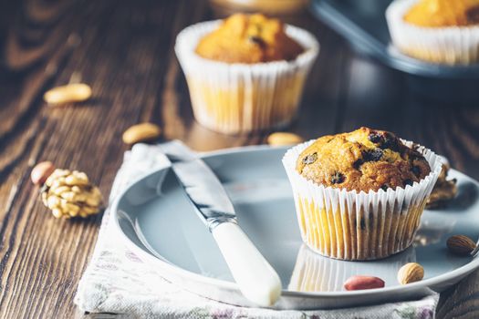 Vanilla caramel muffins in paper cups on plate on dark wooden background. Delicious cupcake with raisins, almonds and nuts. Homemade biscuit cakes. Copy space for text.