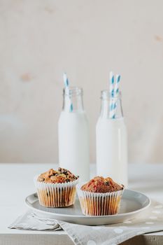 Vanilla caramel muffins in paper cups and botlles of milk on white wooden background. Delicious cupcake with raisins, almonds and nuts. Homemade biscuit cakes. Copy space for text.