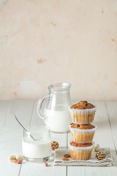 Vanilla caramel muffins in paper cups and glass of milk on white wooden background. Delicious cupcake with raisins, almonds and nuts. Homemade biscuit cakes. Copy space for text.