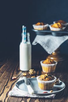 Vanilla caramel muffins in paper cups and bottles of milk on dark wooden background. Delicious cupcake with raisins, almonds and nuts. Homemade biscuit cakes. Copy space for text.