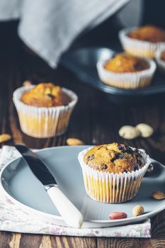 Vanilla caramel muffins in paper cups and bottles of milk on dark wooden background. Delicious cupcake with raisins, almonds and nuts. Homemade biscuit cakes. Copy space for text.