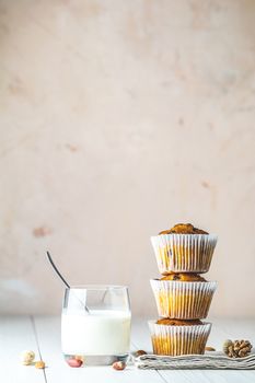 Vanilla caramel muffins in paper cups and glass of milk on white wooden background. Delicious cupcake with raisins, almonds and nuts. Homemade biscuit cakes. Copy space for text.