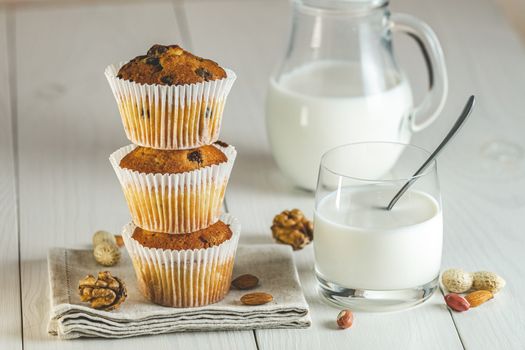 Vanilla caramel muffins in paper cups and glass of milk on white wooden background. Delicious cupcake with raisins, almonds and nuts. Homemade biscuit cakes. Copy space for text.