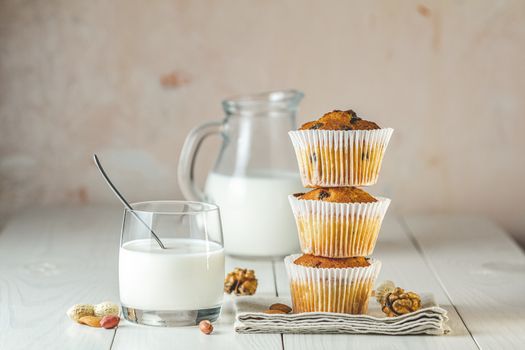 Glass of milk, vanilla caramel muffins in paper cups and bottles of milk on white wooden background. Delicious cupcake. Homemade biscuit cakes.