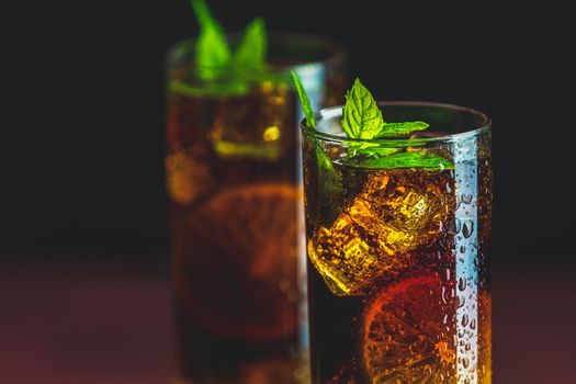 Cold Longdrink Cuba Libre with brown rum and fresh lime in highball glass with water drops on dark background, selective focus