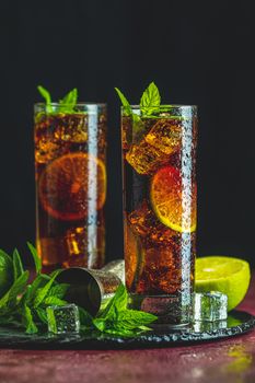 Cold Longdrink Cuba Libre with brown rum and fresh lime in highball glass with water drops on dark background, selective focus