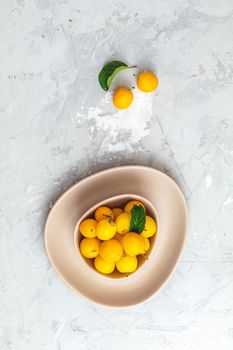 Creative summer pattern made of fresh yellow cherry plums in pink bowl on gray concrete background. Fruit minimal concept. Flat lay.