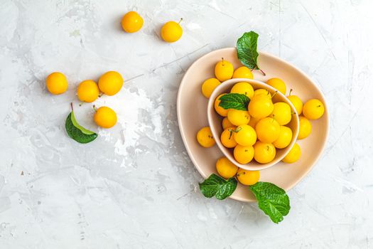 Creative summer pattern made of fresh yellow cherry plums in pink bowl on gray concrete background. Fruit minimal concept. Flat lay.