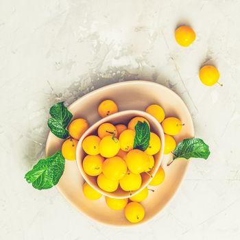 Creative summer pattern made of fresh yellow cherry plums in pink bowl on gray concrete background. Fruit minimal concept. Flat lay.