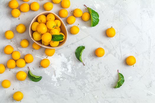 Creative summer pattern made of fresh yellow cherry plums in pink bowl on gray concrete background. Fruit minimal concept. Flat lay.