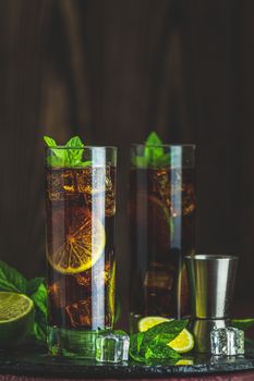 Cold Longdrink Cuba Libre with brown rum and fresh lime in highball glass on dark background, selective focus