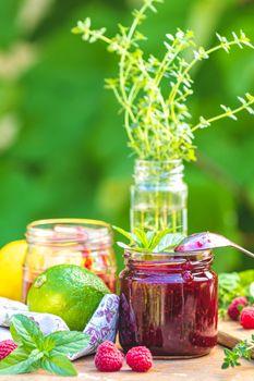 Raspberry jam and fresh raspberry on a rustic wooden table outdoors. Sunny day, green leaves background