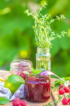 Raspberry jam and fresh raspberry on a rustic wooden table outdoors. Sunny day, green leaves background