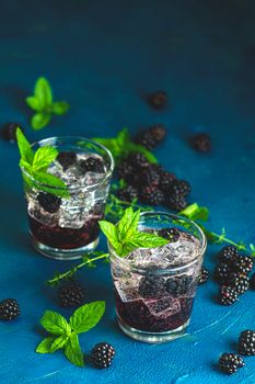 Cold summer berry drink with blackberries. Refreshing summer drink with syrup, blackberry and ice on dark blue concrete background