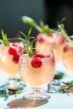 Pink drink with ice. Close up mix berries ice soda with thyme in a transparent glass on white table at cafe.Summer cold Welcome drink and cocktail. Holiday, sunny light