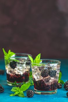 Cold summer berry drink with blackberries. Refreshing summer drink with syrup, blackberry and ice on dark blue concrete background
