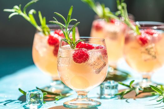 Pink drink with ice. Close up mix berries ice soda with thyme in a transparent glass on white table at cafe.Summer cold Welcome drink and cocktail. Holiday, sunny light