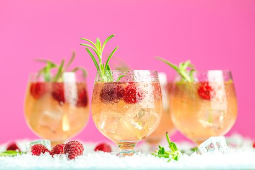 Fresh raspberry cocktail with rosemary and ice in glasses with water drops on pink background. Christmas and New Year holiday welcome drink.