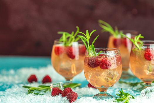 Fresh raspberry cocktail with rosemary and ice in glasses with water drops on dark background. Christmas and New Year holiday welcome drink.