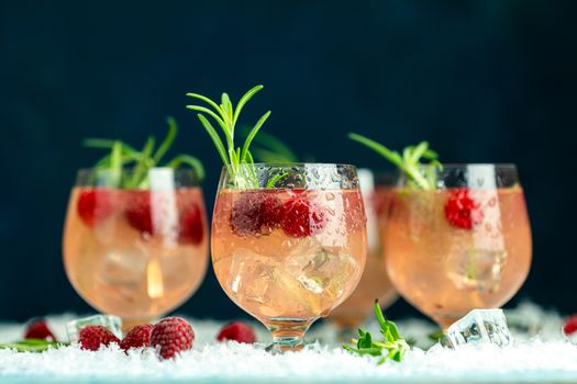 Fresh raspberry cocktail with rosemary and ice in glasses with water drops on dark blue background. Christmas and New Year holiday welcome drink.