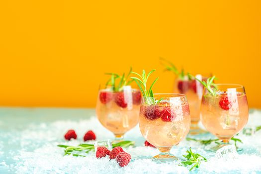 Fresh raspberry cocktail with rosemary and ice in glasses with water drops on yellow background. Christmas and New Year holiday welcome drink.