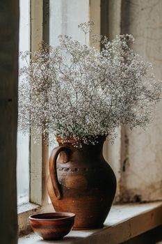 Beautiful retro still life with wild flowers in clay jug on windowsill of an old window. Close up, shallow depth of the field, copy space for you text.