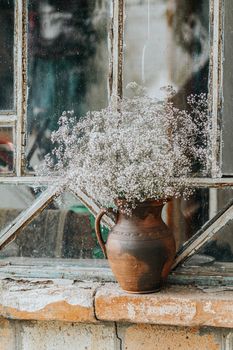 Beautiful retro still life with wild flowers in clay jug on windowsill of an old window. Close up, shallow depth of the field, copy space for you text.