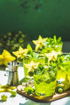 Green gooseberry and carambola cocktail with liqueur, ice and fresh mint on a light gray concrete table. Refreshing summer drink, sunny light. Or detox drink