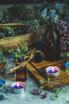 Magic potion in small bottle, blue eryngo and candles on dark background. Old pharmacy, esoteric or alchemic concept. Black magic and occult objects, alternative medicine or homeopathic