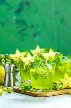 Green gooseberry and carambola cocktail with liqueur, ice and fresh mint on a light gray concrete table. Refreshing summer drink, sunny light. Or detox drink.