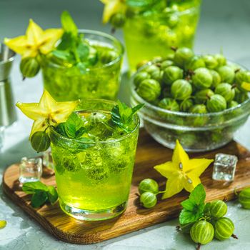 Green gooseberry and carambola cocktail with liqueur, ice and fresh mint on a light gray concrete table. Refreshing summer drink, sunny light. Or detox drink.