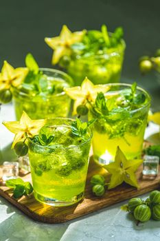 Green gooseberry and carambola cocktail with liqueur, ice and fresh mint on a light gray concrete table. Refreshing summer drink, sunny light. Or detox drink