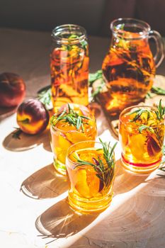 Glasses of sweet peach iced tea, Summer cold peach fizz cocktail with rosemary. Sunny light. Shallow depth of the field, close up, copy space for you text