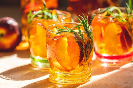 Glasses with drops of sweet peach iced tea, Summer cold peach fizz cocktail with rosemary. Sunny light. Shallow depth of the field, close up, copy space for you text