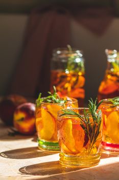 Summer cold peach fizz cocktail or iced tea with rosemary. Sunny light. Shallow depth of the field, close up, copy space for you text.