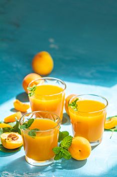 Glass of fresh healthy apricot or peach smoothie or juice on light blue concrete surface table. Sunny light. Shallow depth of the field, close up, copy space for you text