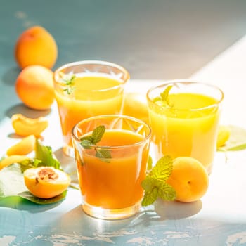 Glass of fresh healthy apricot or peach smoothie or juice on light blue concrete surface table. Sunny light. Shallow depth of the field, close up, copy space for you text