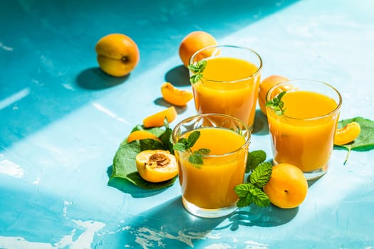Glass of fresh healthy apricot or peach smoothie or juice on light blue concrete surface table. Sunny light. Shallow depth of the field, close up, copy space for you text