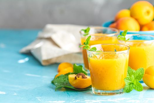 Glass of fresh healthy apricot or peach smoothie or juice on light blue concrete surface table. Sunny light. Shallow depth of the field, close up, copy space for you text