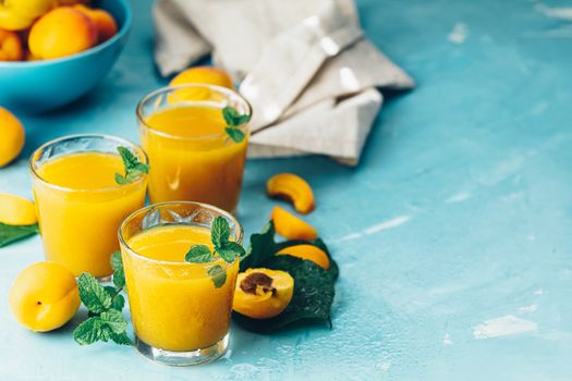 Glass of fresh healthy apricot or peach smoothie or juice on light blue concrete surface table. Sunny light. Shallow depth of the field, close up, copy space for you text