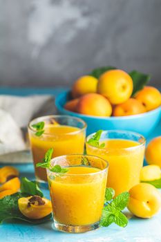 Glass of fresh healthy apricot or peach smoothie or juice on light blue concrete surface table. Sunny light. Shallow depth of the field, close up, copy space for you text