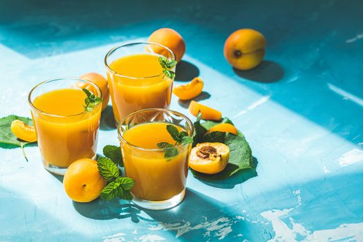 Glass of fresh healthy apricot or peach smoothie or juice on light blue concrete surface table. Sunny light. Shallow depth of the field, close up, copy space for you text
