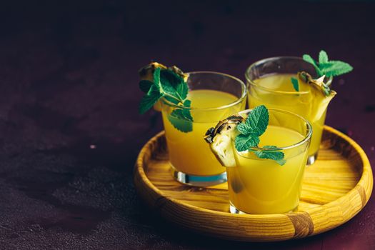 Cold cocktail with squeezed pineapple juice, lime and mint in glasses on concrete surface table. Summer drinks and alcoholic cocktails.