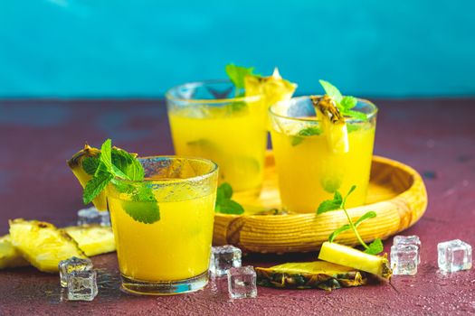 Cold cocktail with squeezed pineapple juice, lime, mint and ice in glasses on concrete surface table. Summer drinks and alcoholic cocktails.
